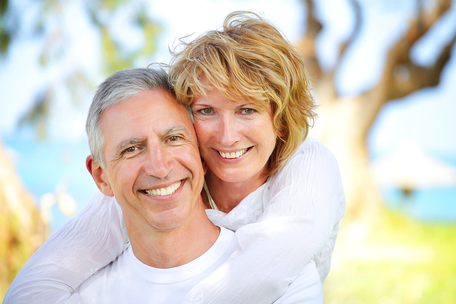 mature couple outdoors near water and trees, smiling nice teeth, dental implants Frederick, MD. 